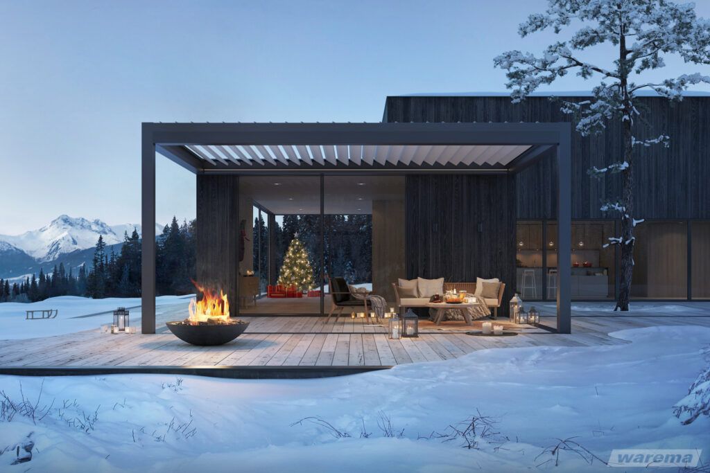 Lamellendach Cubus Lounge an einem Haus mit Feuerstelle umgeben von einer Schneelandschaft